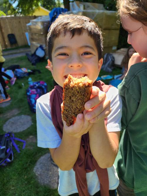 Young, smiling boy holding up a slice of banana bread with a bite missing. 
