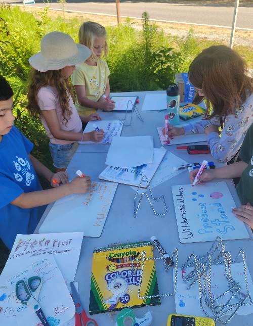 A group of kids is working on various signs to post at their farmstand.